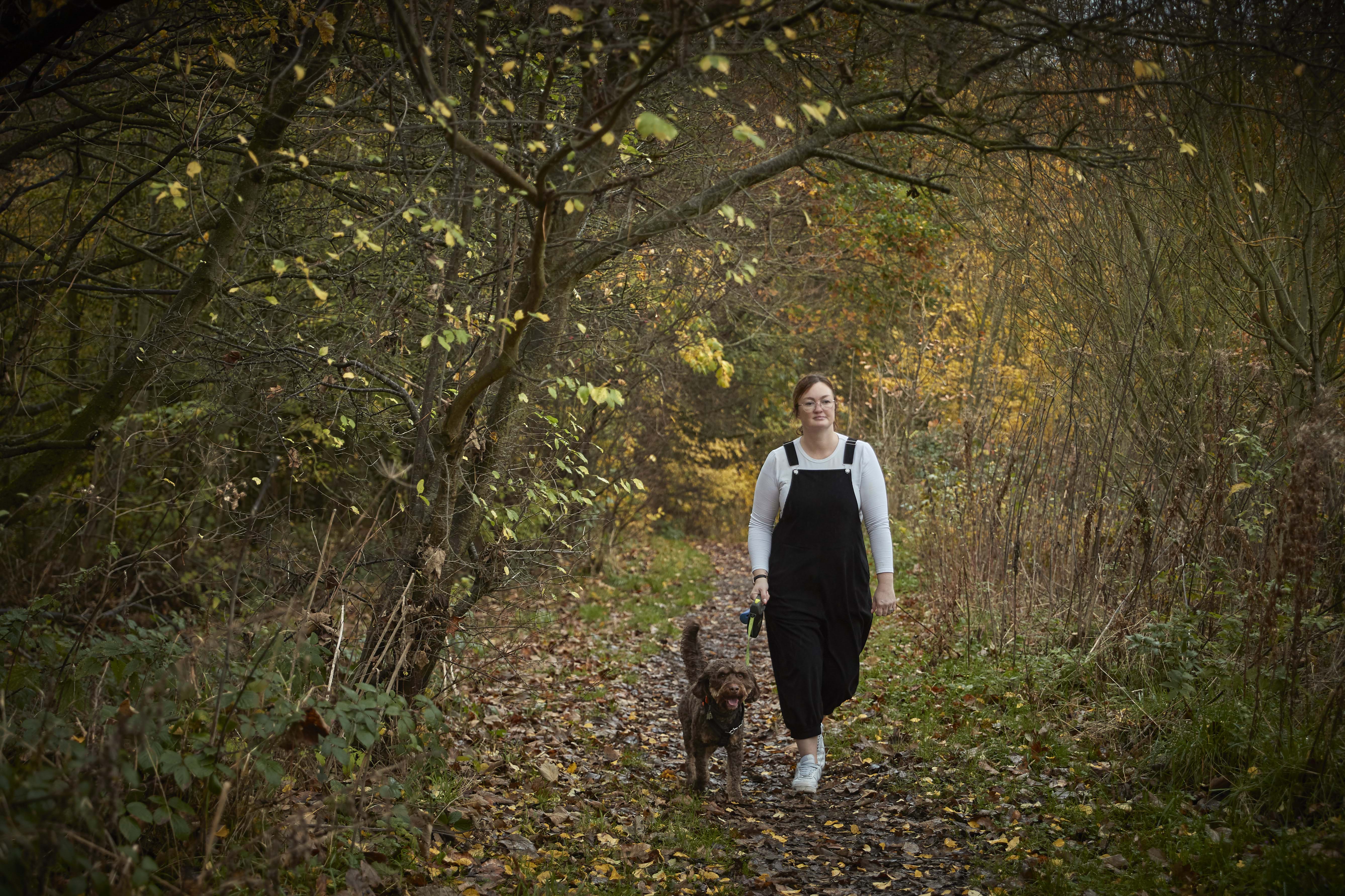 A woman walking a dog in the woods